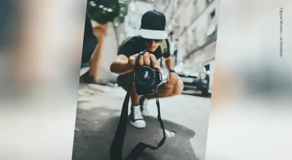 Młody fotograf w czapce z daszkiem trzyma aparat, gotowy do uchwycenia chwili. Zastanawiasz się, ile zarabia fotograf?