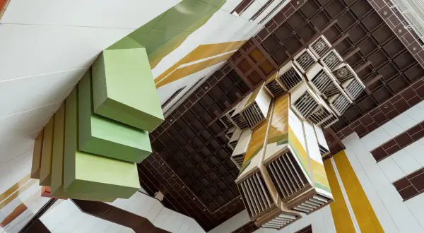 Widok z góry na wnętrze budynku z zielonymi, geometrycznymi formami i kasetonowym sufitem. Fotograf architektury uchwycił unikalną perspektywę.