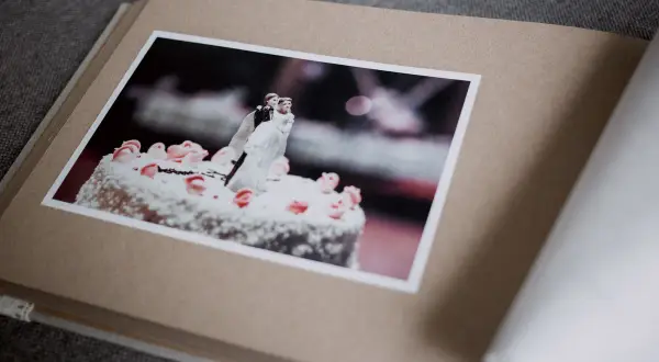 Otwarty album z fotografią tortu weselnego i figurkami pary młodej. Różne rodzaje papieru tworzą jego okładkę i strony.