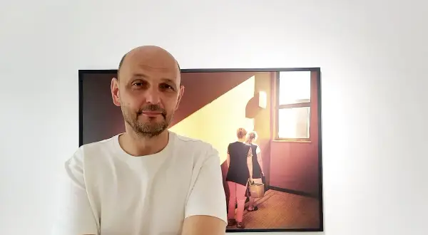 Krzysztof Gołuch obok swojego obrazu z kobietami niosącymi wiadra w świetle.