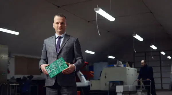Portret mężczyzny w garniturze trzymającego płytkę drukowaną. Wizerunek inaczej ukazuje jego rolę w branży technologicznej.