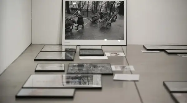 Wystawa prac Chrisa Niedenthala. Na ścianie wisi czarno-białe zdjęcie przedstawiające kobiety pchające wózki. Na podłodze leżą kolejne fotografie.