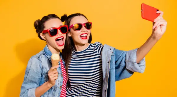 Dwie dziewczyny w okularach przeciwsłonecznych robią sobie selfie z lodami na patyku. Mają świetny pomysł na selfie!