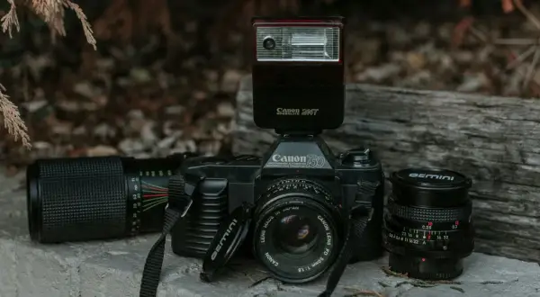 Stary aparat Canon 750 z lampą błyskową Canon Speedlite 244T i obiektywami. Lampa błyskowa inaczej niż współczesne, to retro sprzęt.