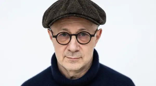 Mikołaj Grynberg w okularach i kaszkiecie, zamyślony, w granatowym golfie.