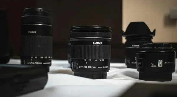 Kilka obiektywów Canon, w tym obiektyw standardowy 50mm i szerokokątny 10-18mm, leży na białej powierzchni.