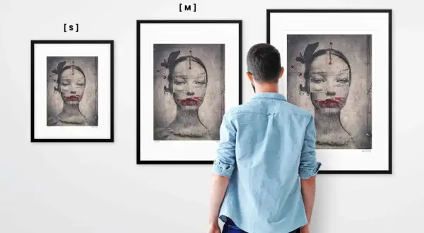 Mężczyzna ogląda trzy obrazy Ewy Ćwikły. Na każdym z nich widnieje surrealistyczny portret kobiety z motylami i czerwonymi ustami.
