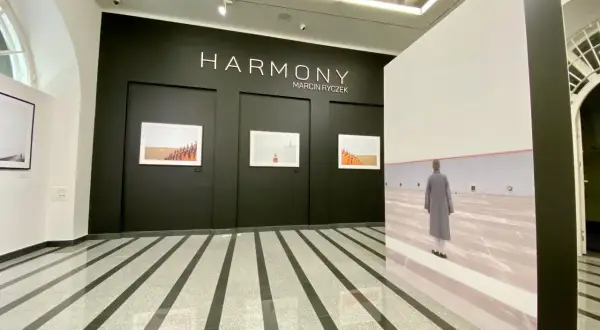 Wystawa "HARMONY" Marcina Ryczka. W galerii widzimy fotografie mnichów i dużą instalację z podobizną postaci w szarym płaszczu.