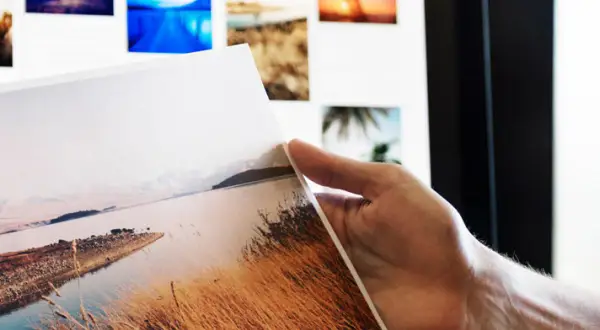 Ręka trzyma wydruk z krajobrazem, na ekranie widać kolejne zdjęcia do portfolio fotografa.