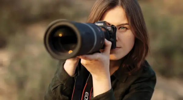 Kobieta z aparatem Canon EOS R7 w rękach, gotowa do uchwycenia idealnego ujęcia. Jej skupienie zdradza pasję do fotografii mody.