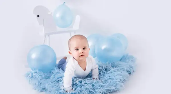 Uroczy niemowlak na niebieskim futerku, otoczony balonami. Idealny pomysł na sesję zdjęciową dziecka w domu.