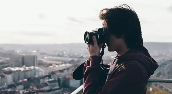 Przeswietlone zdjecie. Młody mężczyzna z aparatem fotograficznym w rękach, robiący zdjęcie miasta z góry.