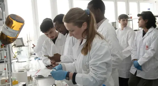 Monika Wanat i studenci w białych fartuchach pracują w laboratorium.