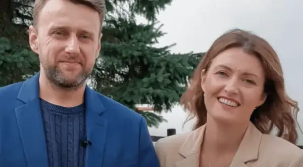 Uśmiechnięty adam kozioł w niebieskiej marynarce obok kobiety w beżowej.