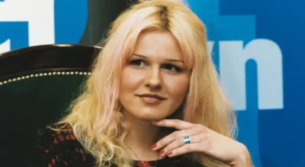 Agnieszka Lorek z blond włosami i delikatnym uśmiechem, oparta o fotel, z ręką podtrzymującą podbródek.