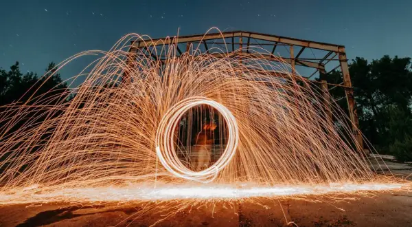 Nocna fotografia z kręcącym się ogniem tworzącym świetlisty okrąg. To definicja kreatywnej fotografii.