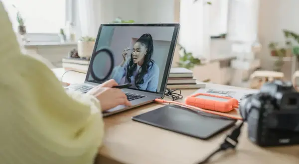 Osoba pracuje przy laptopie, poprawiając makijaż na zdjęciu. W tle widać aparat i dysk zewnętrzny, sugerując pracę nad rozjaśnianiem zdjęć.