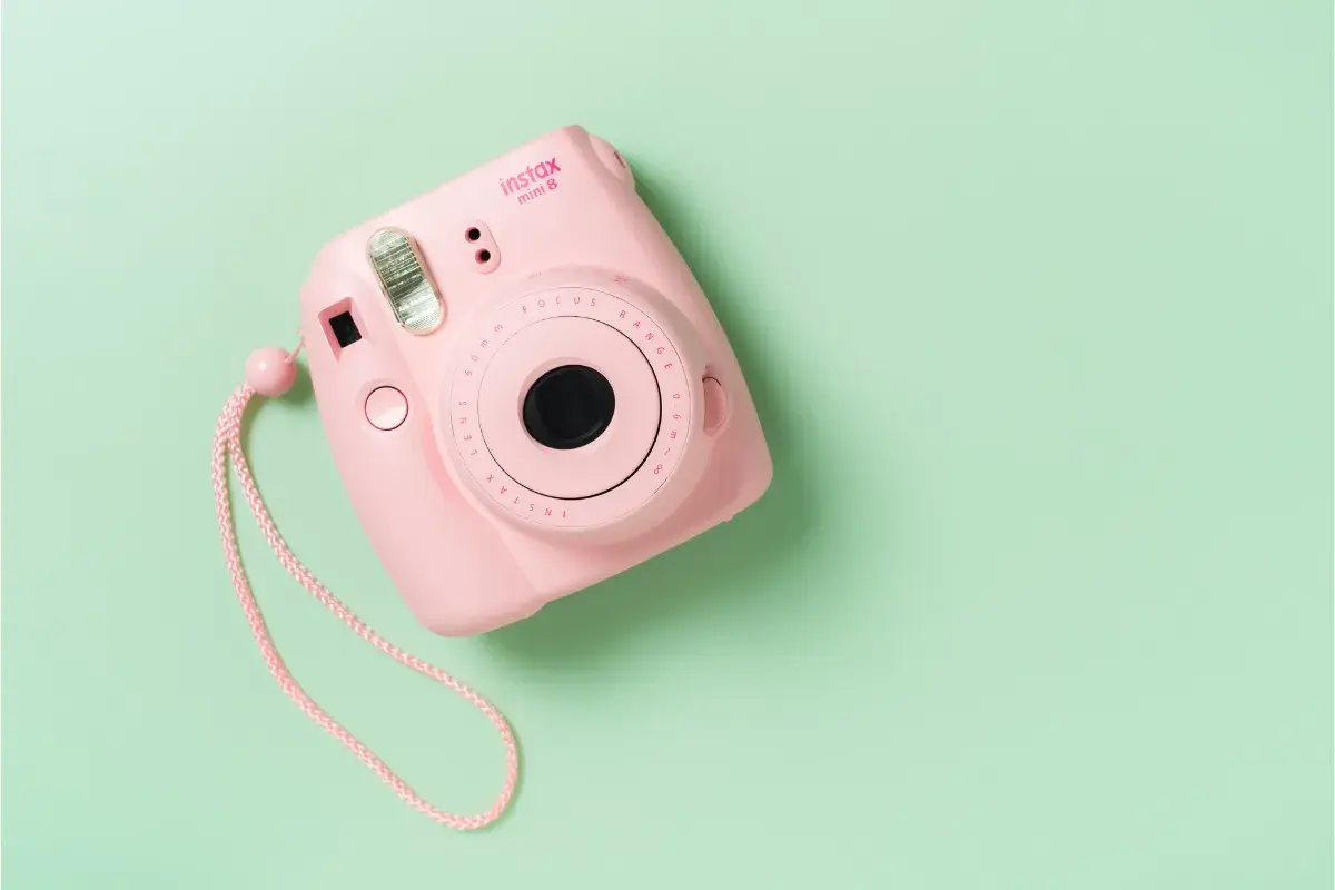 Różowy aparat Instax Mini 8 na pastelowym tle. Dowiedz się, jak działa Instax, tworząc natychmiastowe zdjęcia.
