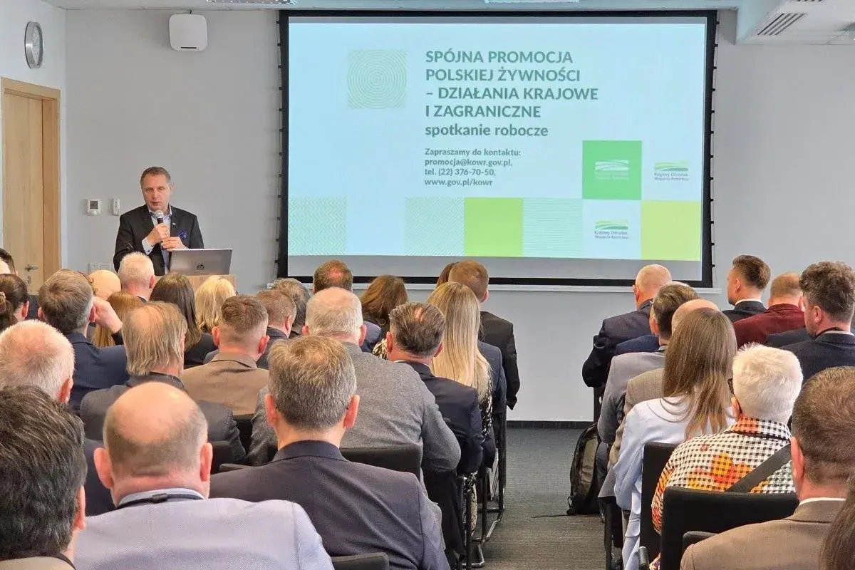 Mężczyzna przemawia na spotkaniu roboczym. Na ekranie widnieje napis "Spójna promocja polskiej żywności". Może to być wada obiektywu, która lekko zniekształca obraz.