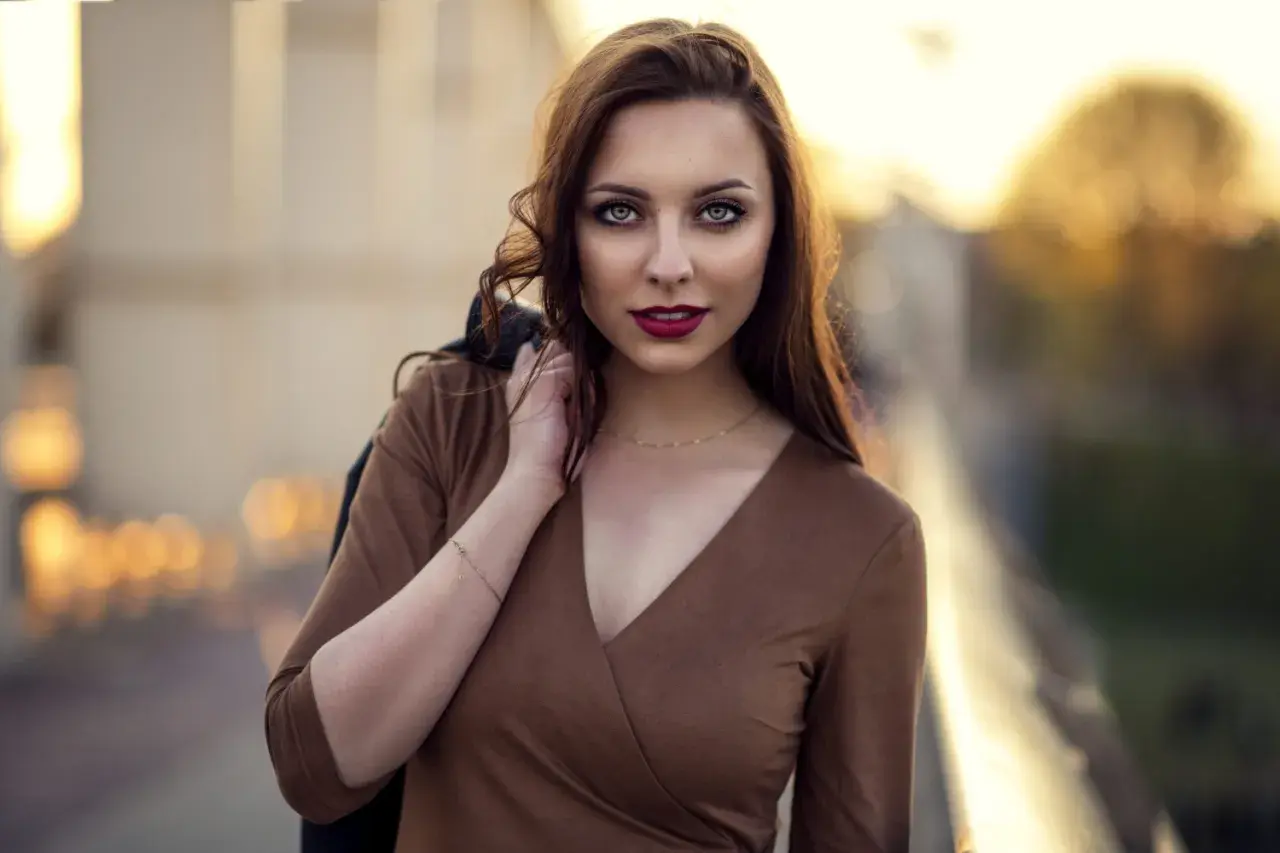 Piękna kobieta w brązowej sukience, z włosami opadającymi na ramię. Jej spojrzenie przyciąga uwagę w tej subtelnej fotografii portretowej.