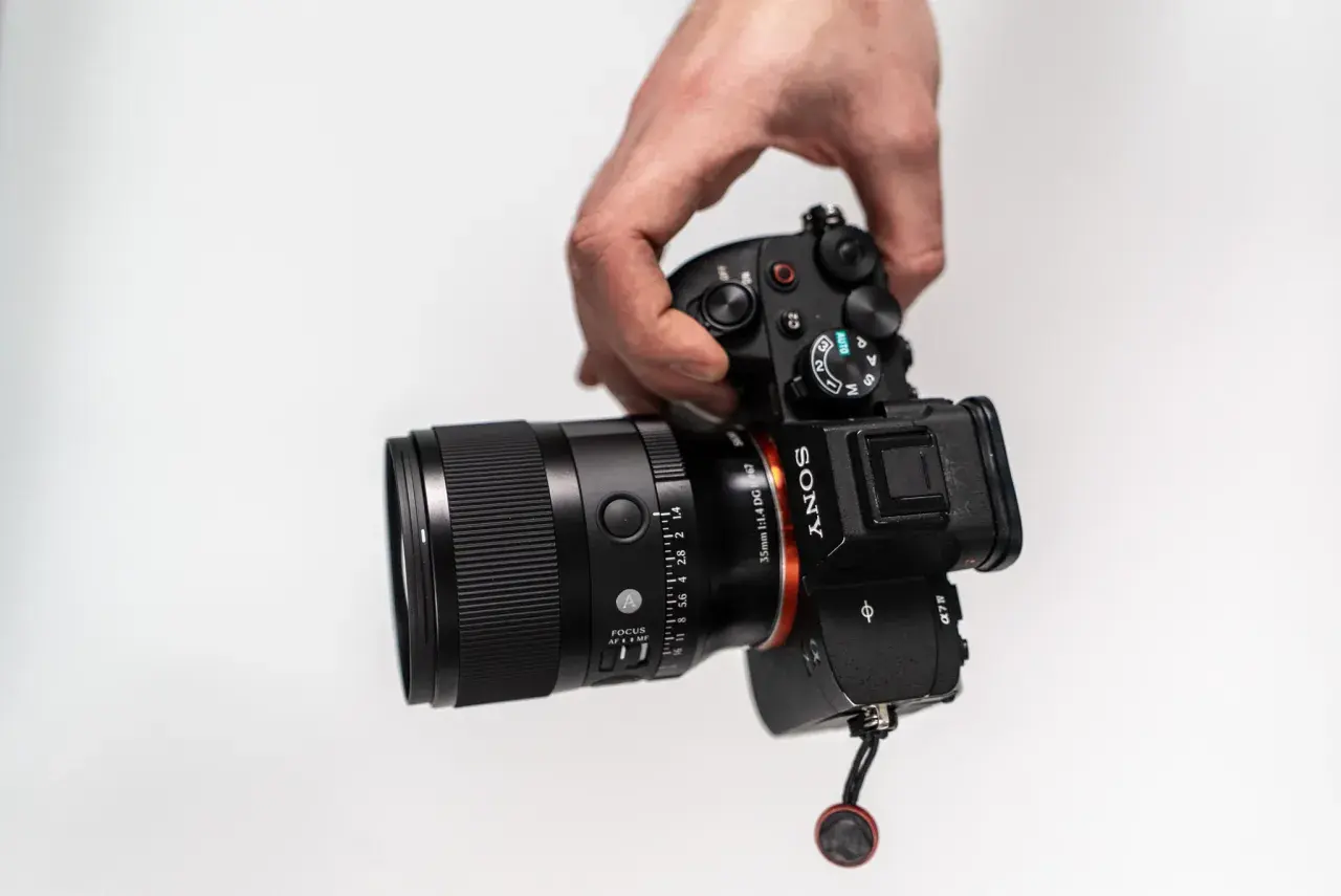 Dłoń trzyma aparat Sony z obiektywem 35 mm f/1.4. Idealny do portretów i krajobrazów, ten obiektyw 35 mm do czego służy?