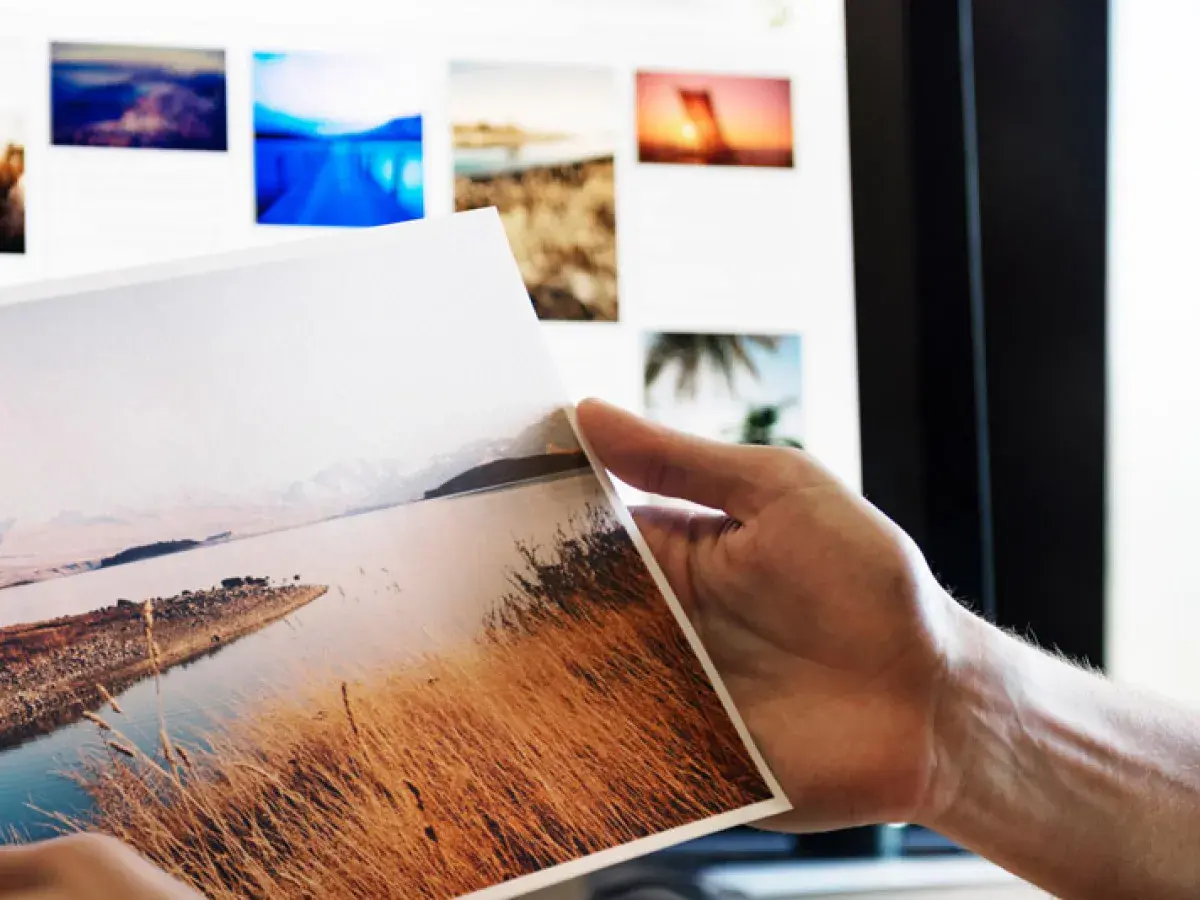 Ręka trzyma wydruk z krajobrazem, na ekranie widać kolejne zdjęcia do portfolio fotografa.