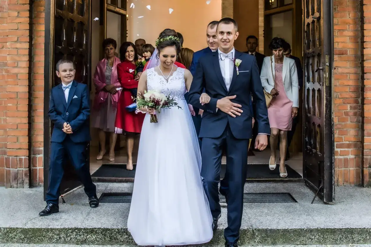 Szczęśliwa para młoda, Jakub Walczak i jego żona, wychodzą z kościoła, obsypani płatkami.