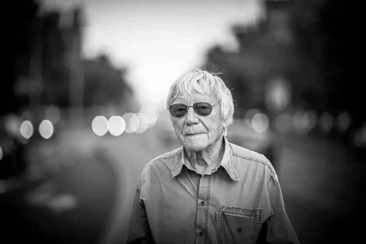 Portret starszego mężczyzny w okularach, z siwymi włosami, w koszuli. To Tadeusz Rolke, ikona polskiej fotografii.