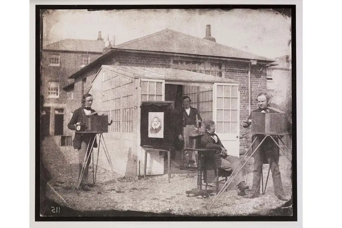 William Fox Talbot w otoczeniu aparatów i modeli, w tym portretu, w plenerowym studiu fotograficznym.