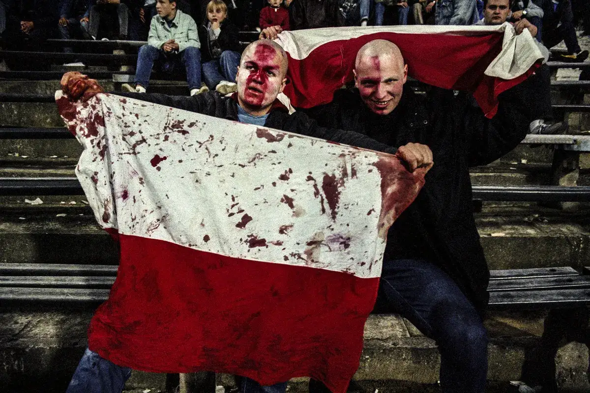 Dwóch mężczyzn z zakrwawionymi twarzami trzyma polską flagę. Mariusz Forecki uchwycił ten moment.