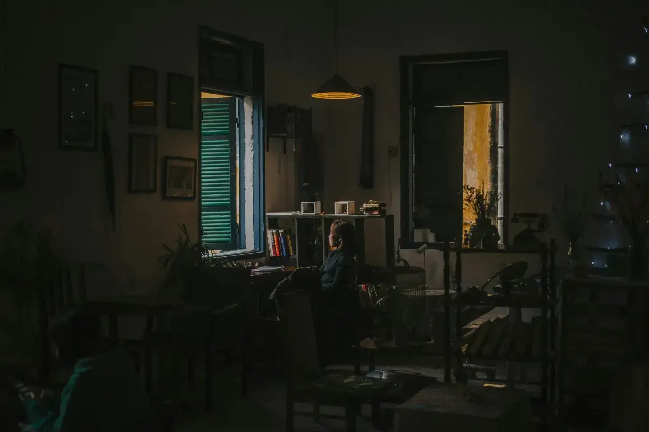 Kobieta siedzi przy oknie, wpatrując się w światło. W pokoju panuje półmrok, jak w ciemni fotograficznej, gdzie powstaje roztwór.