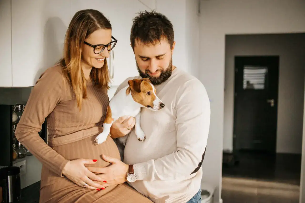 Szczęśliwa para podczas sesji ciążowej z psem. Przyszli rodzice czule trzymają swojego pupila, wyczekując na przyjście dziecka.