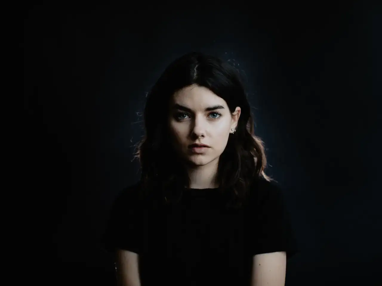 Młoda kobieta z niebieskimi oczami, idealna modelka na kurs fotografii portretowej. Ciemne tło podkreśla jej urodę.