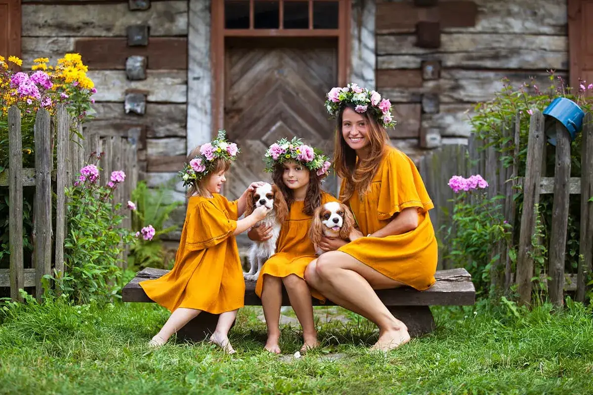 Wiosenna sesja dzieci z mamą i pieskami. Dziewczynki w wiankach i żółtych sukienkach, przytulają cavalier king charles spaniele.