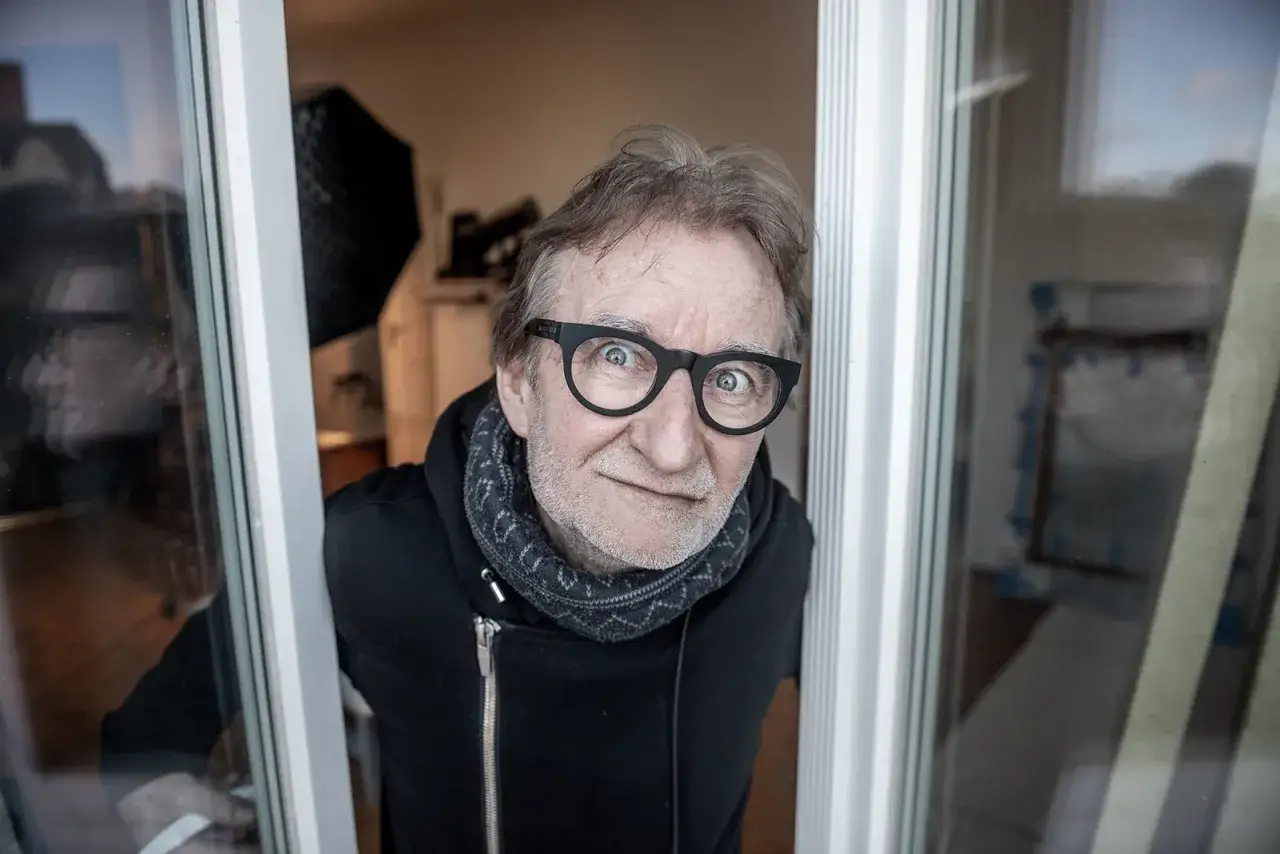 Maciej Mańkowski w okularach, z zaciekawieniem spogląda przez okno.