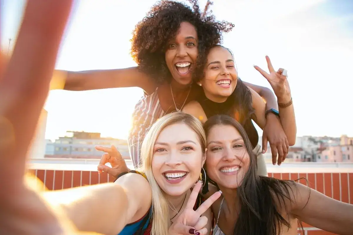 Czwórka uśmiechniętych przyjaciółek robi sobie selfie na dachu. To świetny pomysł na selfie, pełne radości i słońca.