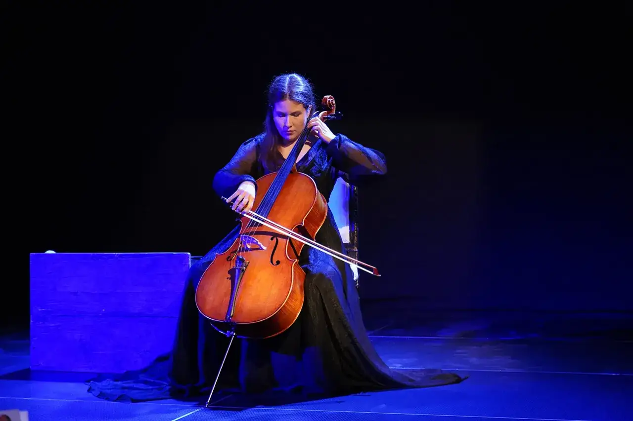 Kobieta gra na wiolonczeli na scenie. Ta fotografia teatralna uchwyciła moment artystycznego wykonania.