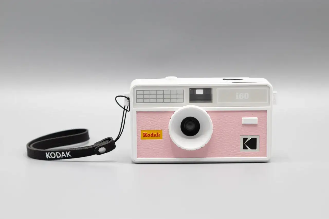 Różowy aparat Kodak i60, pierwszy aparat małoobrazkowy, z czarną smyczą z logo Kodak.