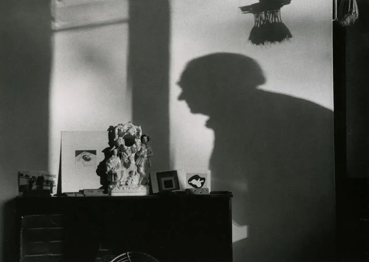 Cień Andre Kertesz na ścianie, obok ozdobnej figurki i przedmiotów na kominku.