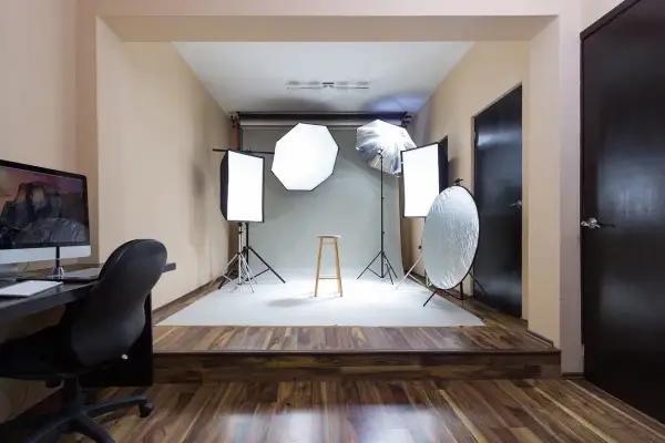 Gotowy pokój fotografa: lampy, statywy, taboret i komputer czekają na sesję.
