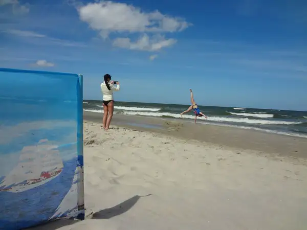 Dziewczyna robi zdjęcie akrobatce na plaży. W tle widać morze i chmury, a horyzont jest lekko krzywy.