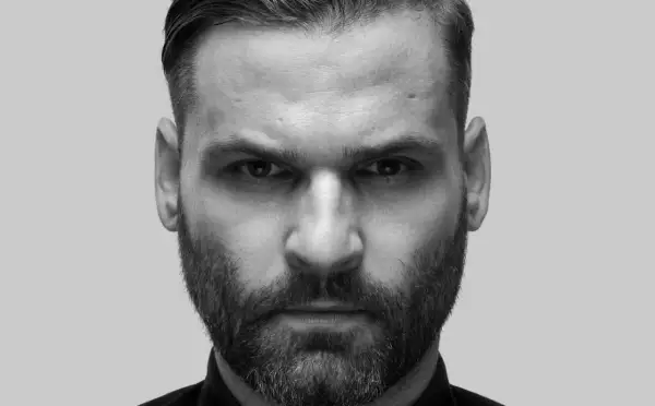 Intensywne spojrzenie Karola Grygoruka w czarno-białym kadrze. Mężczyzna z zarostem i zaczesanymi włosami patrzy prosto w obiektyw.