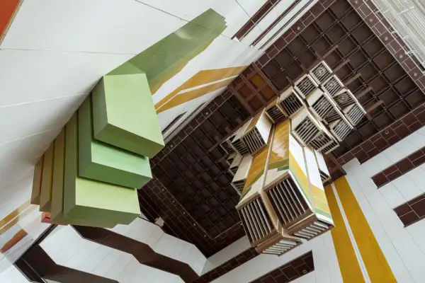 Widok z góry na wnętrze budynku z zielonymi, geometrycznymi formami i kasetonowym sufitem. Fotograf architektury uchwycił unikalną perspektywę.