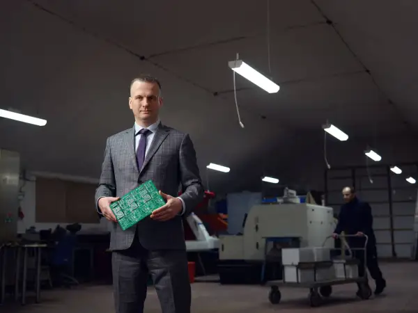 Portret mężczyzny w garniturze trzymającego płytkę drukowaną. Wizerunek inaczej ukazuje jego rolę w branży technologicznej.