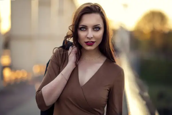 Piękna kobieta w brązowej sukience, z włosami opadającymi na ramię. Jej spojrzenie przyciąga uwagę w tej subtelnej fotografii portretowej.
