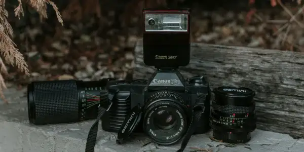 Stary aparat Canon 750 z lampą błyskową Canon Speedlite 244T i obiektywami. Lampa błyskowa inaczej niż współczesne, to retro sprzęt.