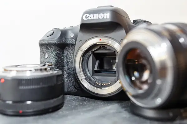Aparat Canon z odłączonym obiektywem i dwoma innymi akcesoriami, które mogą wpływać na ekwiwalent ogniskowej.