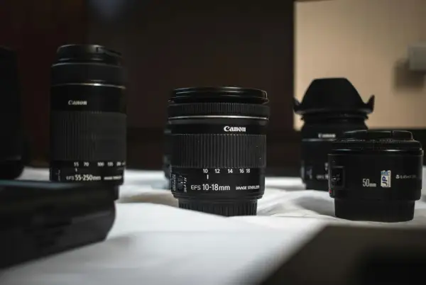 Kilka obiektywów Canon, w tym obiektyw standardowy 50mm i szerokokątny 10-18mm, leży na białej powierzchni.