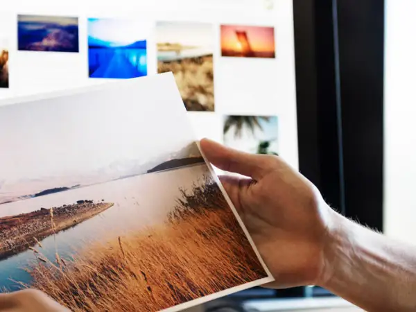 Ręka trzyma wydruk z krajobrazem, na ekranie widać kolejne zdjęcia do portfolio fotografa.