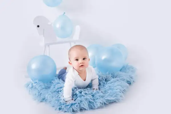 Uroczy niemowlak na niebieskim futerku, otoczony balonami. Idealny pomysł na sesję zdjęciową dziecka w domu.
